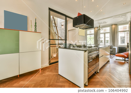 a modern kitchen with wood flooring and white cabinets in the center of the room is an open door leading to the living area 106404992