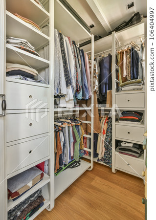 a walk - in closet with lots of clothes hanging on the walls and drawers below it is an example of how to organize your wardrobes 106404997