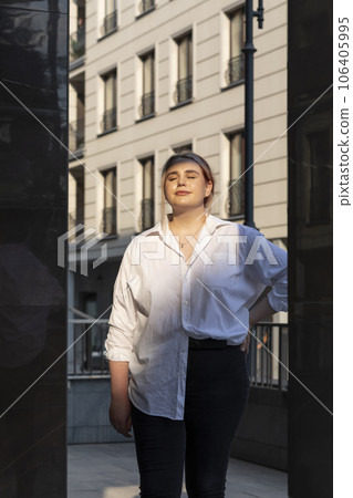 Portrait Beautiful Feminine Plus Size 20s Woman, Gentle Zoomer With Closed Eyes and Light Smile, Sunlight and Shadow. Modern Building on Background. Young Relaxed Caucasian Female Of Gen Z. Vertical. 106405995