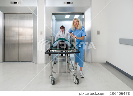 A nurse and doctor in propels a wheeled stretcher, carrying a patient out of the elevator to the emergency room of the hospital. 106406478