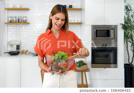 A health-conscious woman embracing a wholesome lifestyle, stands in her inviting kitchen, her hands gently cradling a vibrant, colorful bowl of salad, symbolic of her commitment to nutrition. 106406485