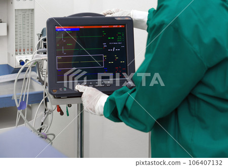 Multi-parameter patient monitor in operating room, controlled by nurse in surgical green gown uniform. Multi-parameter patient monitor in operating room, controlled by nurse in surgical green gown uniform. 106407132