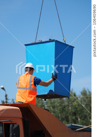 Handyman in protective vest and hard hat unloads garbage can into back of truck on summer day Handyman in protective vest and hard hat unloads garbage can into back of truck on summer day 106409690