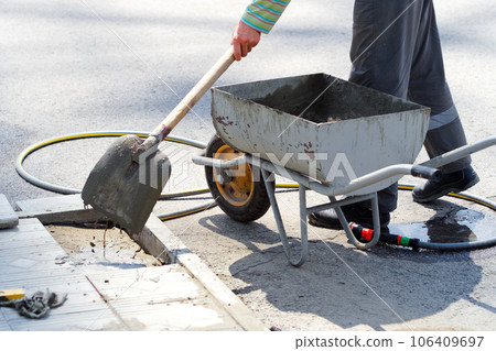 Worker lays foundation tiles of house. View of shovel with liquid cement. Builder repairing pavement Worker lays foundation tiles of house. View of shovel with liquid cement. Builder repairing pavement 106409697