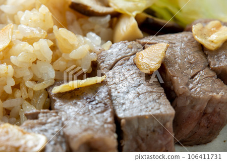 咬一口牛排的特寫鏡頭。一盤蒜蓉飯。 106411731