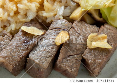 A close-up of a bite of steak. One plate with garlic rice. 106411734
