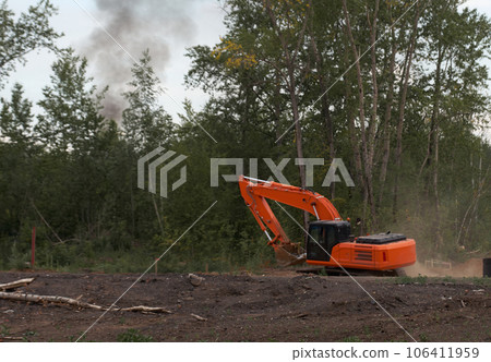Orange excavator in a cloud of dust works at a construction site 106411959