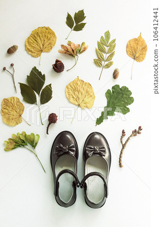 Black childrens boots fall foliage on a white background top view. School uniform shoes for girls. Autumn flatlay Black childrens boots fall foliage on a white background top view. School uniform shoes for girls. Autumn flatlay 106412441
