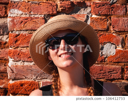 Young woman in straw hat portrait on red brick wall urban background Pretty millennial girl walks on summer city street 106412733