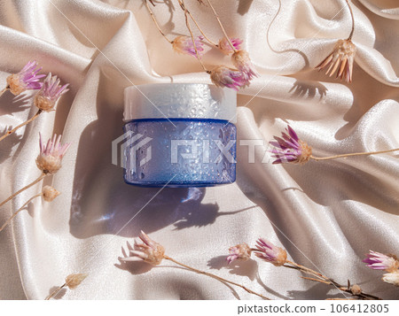 Blue glass cream jar on smooth silk background in sunlight flowers shadows. Natural skincare moisturizer cosmetic mockup Blue glass cream jar on smooth silk background in sunlight flowers shadows. Natural skincare moisturizer cosmetic mockup 106412805