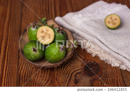 Green feijoa in a coconut shell hulf on a wooden background. Ripe tropical fruits, raw vegan food.Vitamin C. Copy space. 106412855
