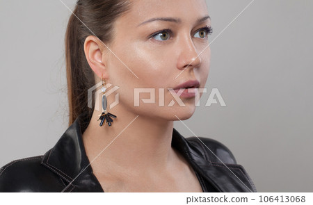 Gold and black earring on ear of glamorous woman 106413068