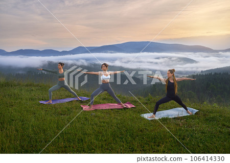 Sporty young women in activewear doing yoga exercises with view on summer mountains. Concept of people, flexibility and meditation. 106414330