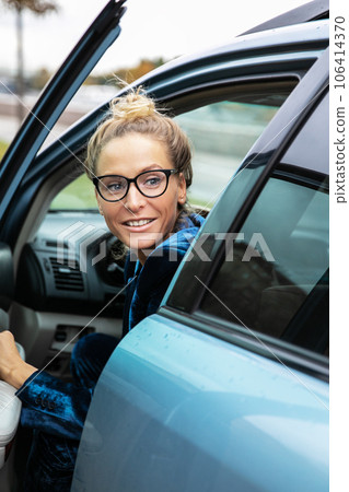 Blonde woman with glasses look back over her shoulder she get out of parked car in which she drove 106414370