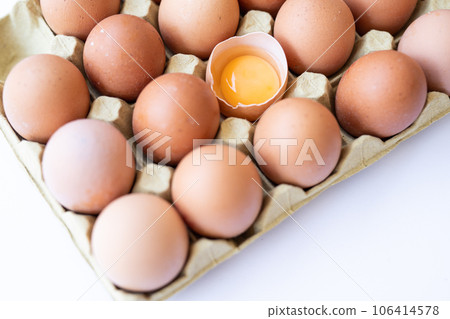 Fresh chicken brown eggs in a tray on a white background. Broken egg with yolk inside the shell. 106414578