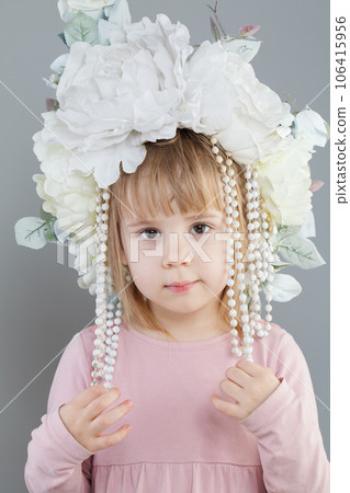 Little girl wearing white flower hat looking at camera on gray background 106415956