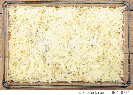 Unsweetened burek sprinkled with grated cheese in a glass baking dish on a wooden background. 106418735