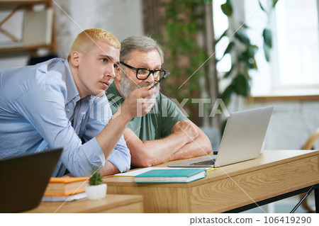 Young guy, employee working with senior man and discussing with him business equations. Assistance and cooperation Young guy, employee working with senior man and discussing with him business equations. Assistance and cooperation 106419290