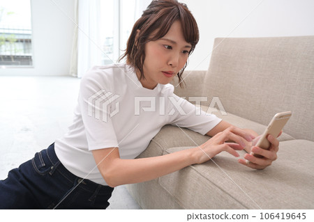 A woman leaning on a sofa and operating a smartphone A woman leaning on a sofa and operating a smartphone 106419645