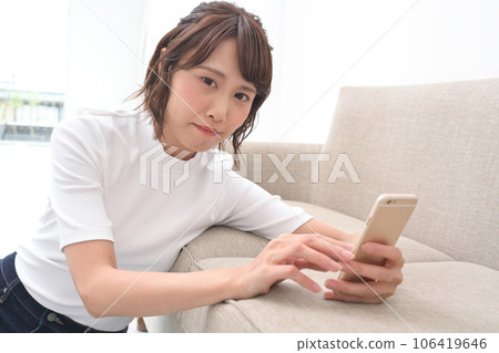 A woman leaning on a sofa and operating a smartphone A woman leaning on a sofa and operating a smartphone 106419646