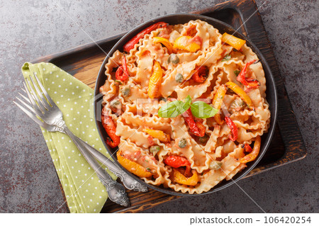 Mafaldine also known as reginette or simply mafalda or mafalde pasta in Creamy Tomato Sauce with capers and baked papper closeup on the plate. Horizontal top view 106420254