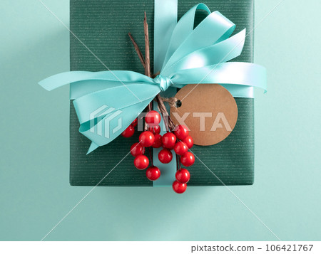 Part of green gift box with turquoise ribbon, craft gift tag and red berries. Turquoise background. Part of green gift box with turquoise ribbon, craft gift tag and red berries. Turquoise background. 106421767