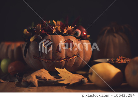 Halloween pumpkin decorated with flowers and gummy eyes on a wooden table. Conceptual still life of Halloween. 106423294