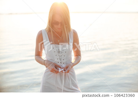 Young attractive Woman in White Dress at Sea Beach on Sunset, sunny Summer Fashion Style, vacation. Young attractive Woman in White Dress at Sea Beach on Sunset, sunny Summer Fashion Style, vacation. 106423360