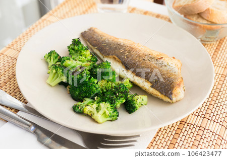 Fried fillet of sea bass with garnish of broccoli on black warm stone plate 106423477