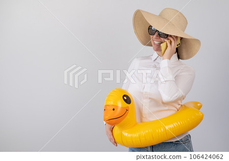 Caucasian woman talking on the phone in sunglasses, a hat and a duck in a swim ring.  106424062