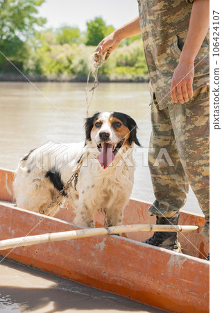 Excited dog travelling with male owner in old red boat on summer vacation. Portrait of funny irish setter enjoying vessel trip, while sticking out tongue and looking at camera. Concept of trip.  106424107