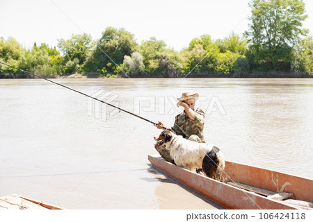 Exhausted male angler with dog, wiping sweat from forehead with hand, while catching fish from boat. Front view of tired guy with fishing pole fishing on lake in hot day. Pleasant tiredness concept. Exhausted male angler with dog, wiping sweat from forehead with hand, while catching fish from boat. Front view of tired guy with fishing pole fishing on lake in hot day. Pleasant tiredness concept. 106424118