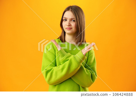 Teen girl shows cross hands gesture, rejecting something over yellow background in studio 106424888