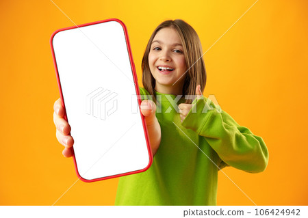 Teen girl showing smartphone screen with copy space over yellow background Teen girl showing smartphone screen with copy space over yellow background 106424942