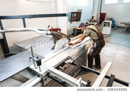 Young carpenter cutting a piece of wood in using a circular saw in furniture factory Young carpenter cutting a piece of wood in using a circular saw in furniture factory 106424999