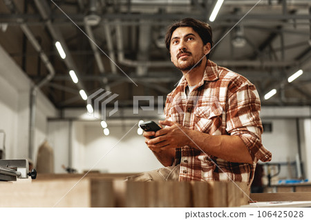 Young carpenter using his mobile phone in workshop Young carpenter using his mobile phone in workshop 106425028