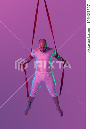Athletic man in a white sport suit is performing an acrobatic elements in a studio. 106425707