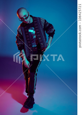 Studio shot of a young tattoed bald man posing against a colorful background. 90s style. Studio shot of a young tattoed bald man posing against a colorful background. 90s style. 106425721