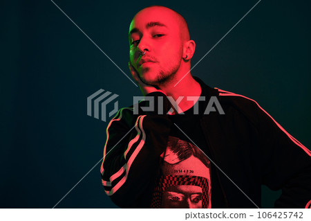 Studio shot of a young tattoed bald man posing against a colorful background. 90s style. 106425742