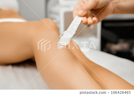 The beautician applying the cream with wax on female legs in beauty salon The beautician applying the cream with wax on female legs in beauty salon 106426465