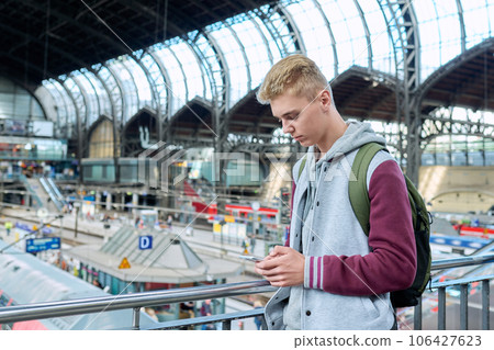 Young guy using mobile apps on smartphone standing at railway station Young guy using mobile apps on smartphone standing at railway station 106427623