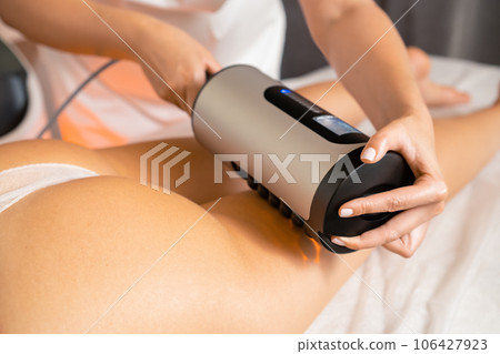 Vibrational anti-cellulite therapy massage device for figure correction in spa salon. Professional cosmetologist works with woman figure correction 106427923