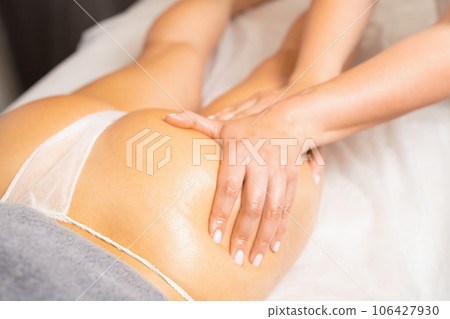 Anti-cellulite massage in luxury spa salon. Professional masseur massaging buttocks with hands in oil to woman client in beauty spa salon 106427930