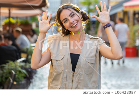 Young woman smiling friendly at camera, waving hands hello, hi, greeting or goodbye on city street 106428087