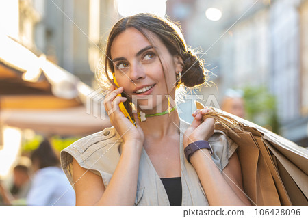 Woman shopaholic consumer after shopping sale with full bags with gifts outdoors, talking on phone Woman shopaholic consumer after shopping sale with full bags with gifts outdoors, talking on phone 106428096