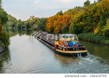 Transportation industry. Ship barge transports scrap metal and sand with gravel. Barge loaded with scrap metal is on the roadstead. Scrap metal transportation by water. Barge laden by metal salvage 106428749