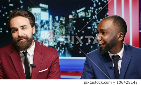 Diverse men start late night show in studio, presenters talking about latest scandals or important daily events on live program. Team of journalists creating media entertainment segment at talk show. 106429142
