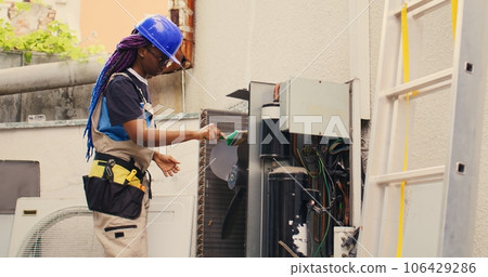 Qualified electrician commissioned by home owner for annual air conditioner routine maintenance, using soft dusting brush to clean dirty condenser coils and filters, outdoor 106429286
