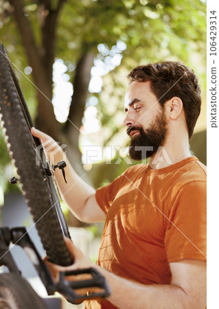 Outdoor detailed shot of caucausian man securing and adjusting bike tire rubber for annual maintenance. Healthy male cyclist dismantling damaged bicycle wheel to repair with expert work tool for 106429314