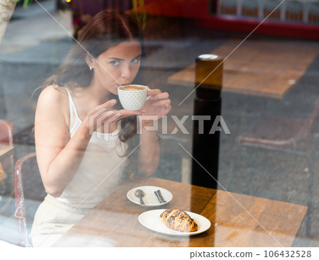 Portrait of young female at table in a cafe, drinking coffee from cup Portrait of young female at table in a cafe, drinking coffee from cup 106432528